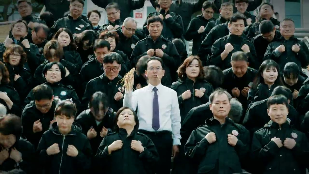 韓國榮州市副市長手拿人蔘站在中央,身後數十名穿黑色制服的主管公務員在階梯上整齊跳舞